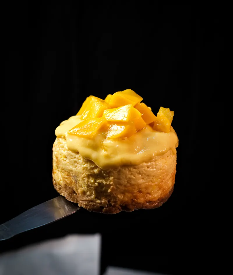 Mango cheesecake on a spatula with a dark background
