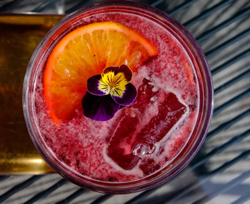 Red drink with orange and an edible flower, seen from above