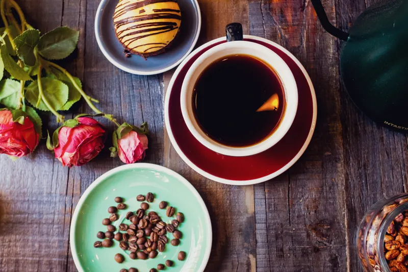 Taza de café negro con rosas y granos